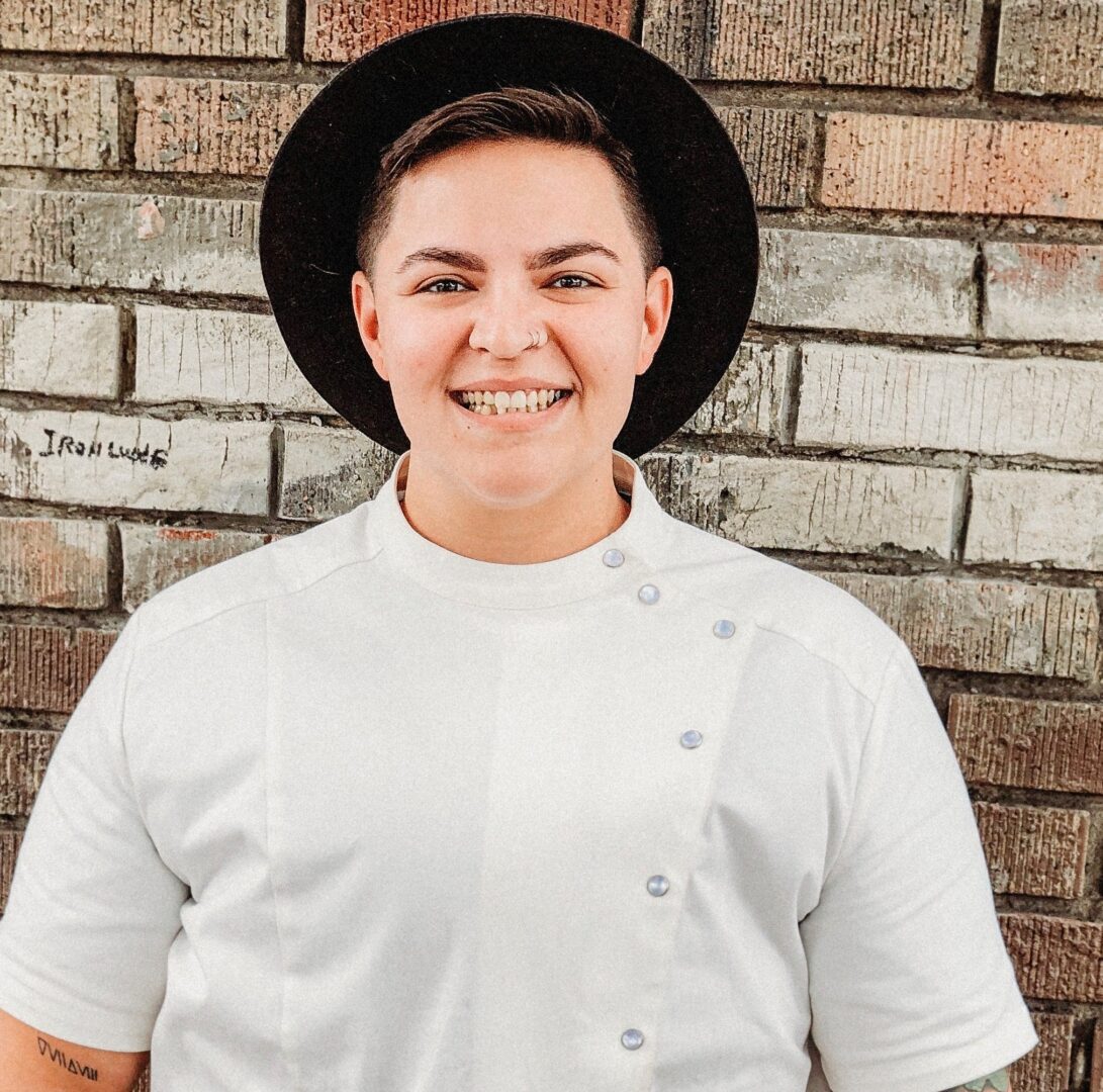 A person wearing a hat standing in front of a brick wall.